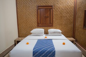 A neatly made bed with white linens and a blue patterned bedspread, flanked by two wooden nightstands with white pillows. - Geringsing Bungalow (Karangasem)