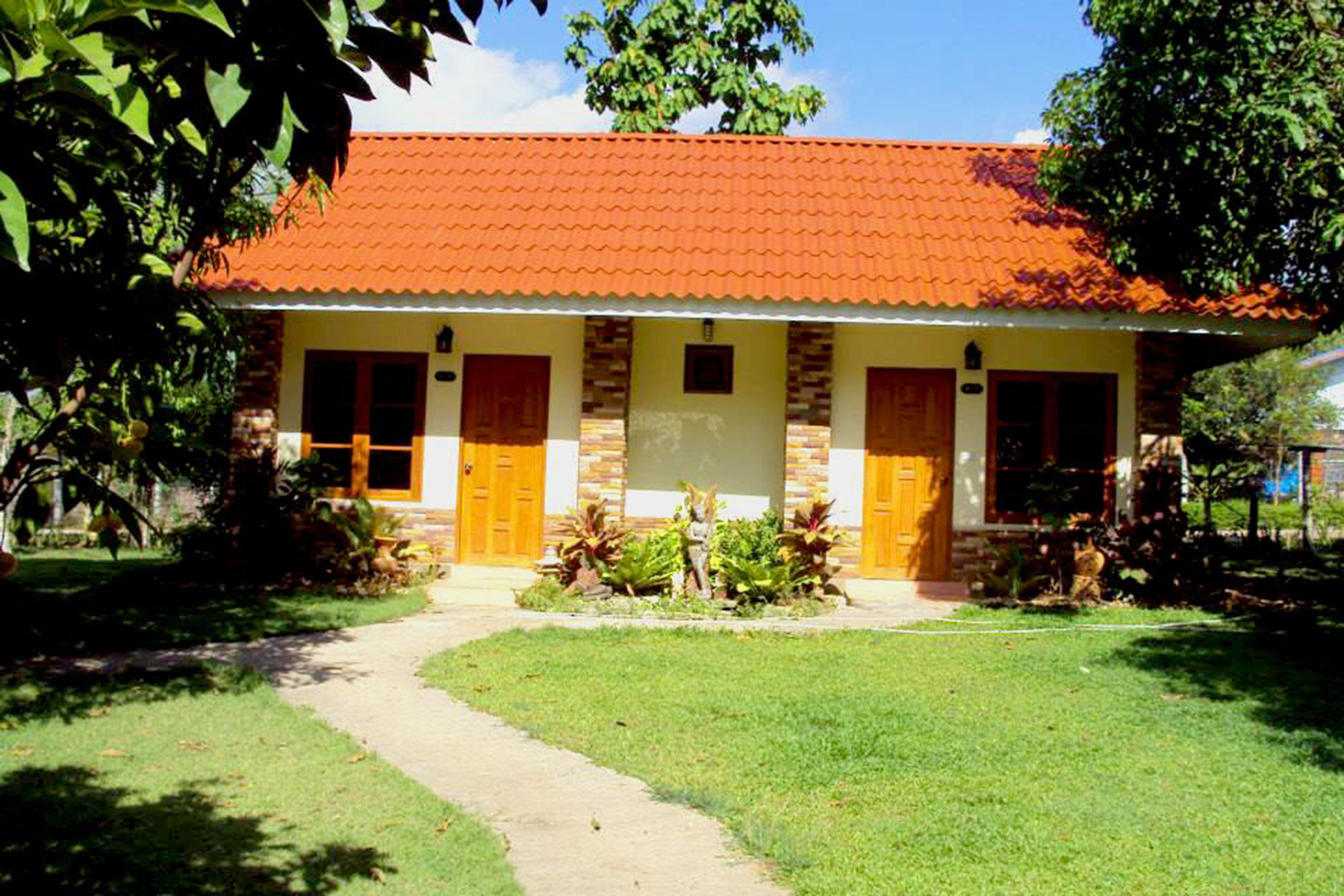 A two-story building with a red-tiled roof, a central entrance, and a small garden area with plants.