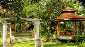 A gazebo with a wooden roof and a white structure with a wooden frame in a lush garden. - Baan Phuthadol (Mae Hong Son)