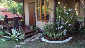 A house with a mushroom-shaped roof, a wooden door, and a garden with various plants. - Baan Phuthadol (Mae Hong Son)