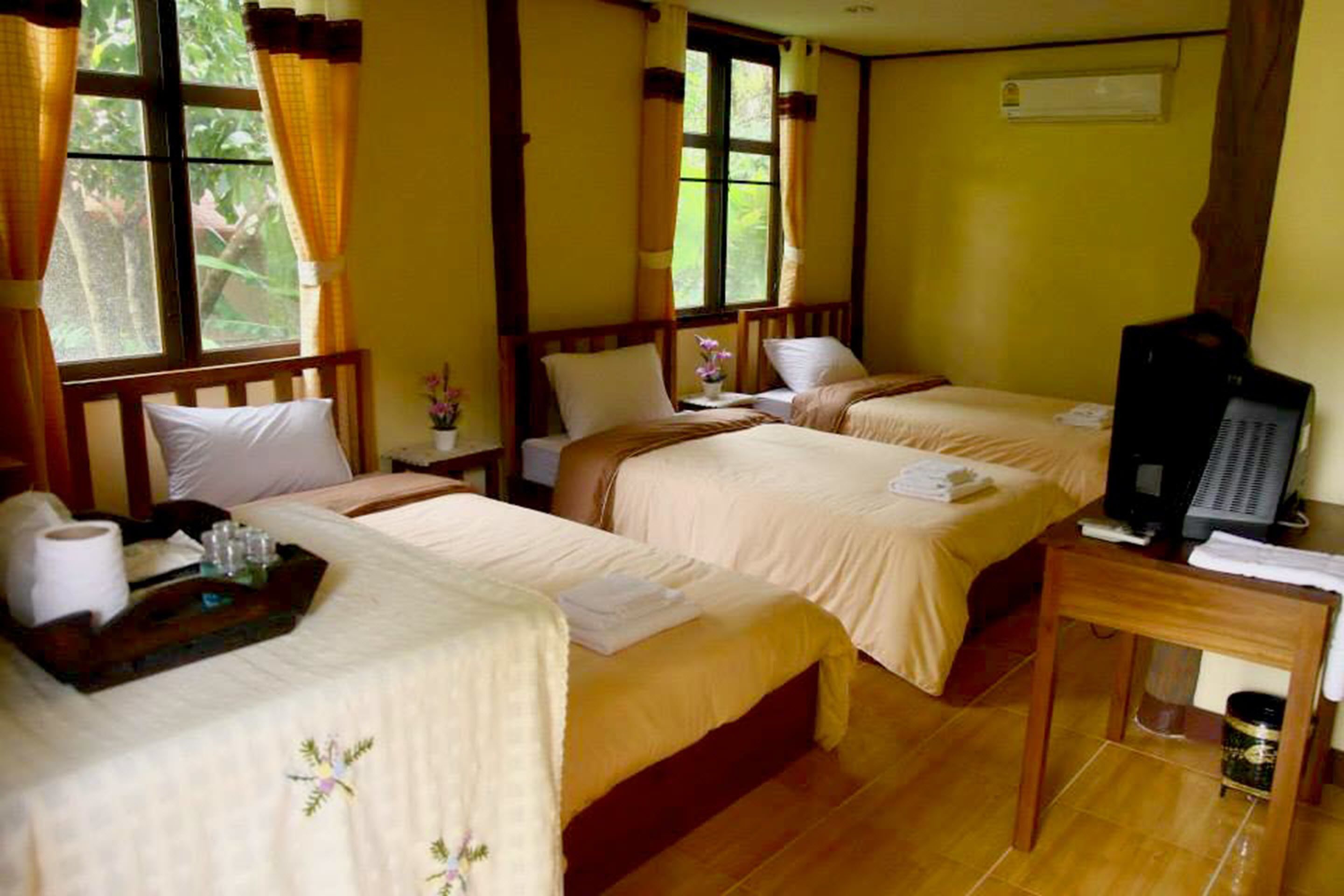 A hotel room with two beds, a wooden desk with a television, and a window with curtains.