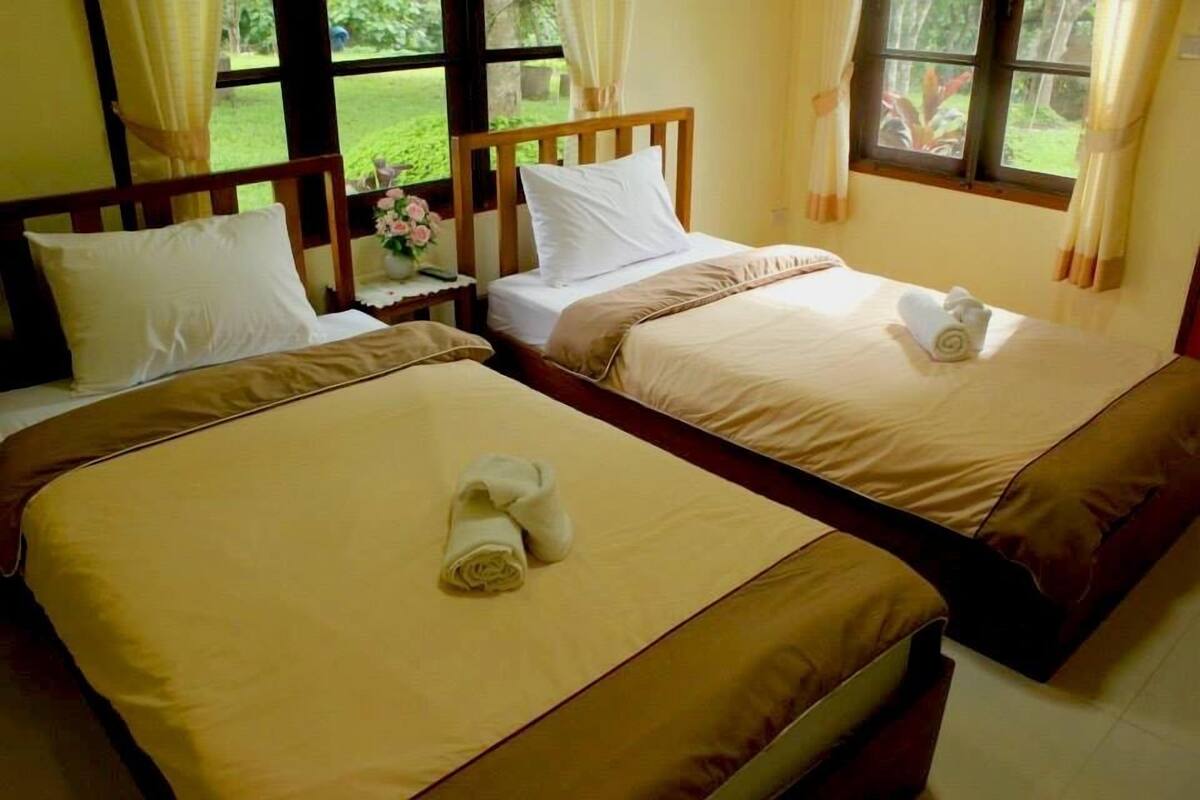 Deux lits simples avec des têtes de lit en bois, une literie beige et des oreillers blancs. Chaque lit est agrémenté d’une serviette roulée.