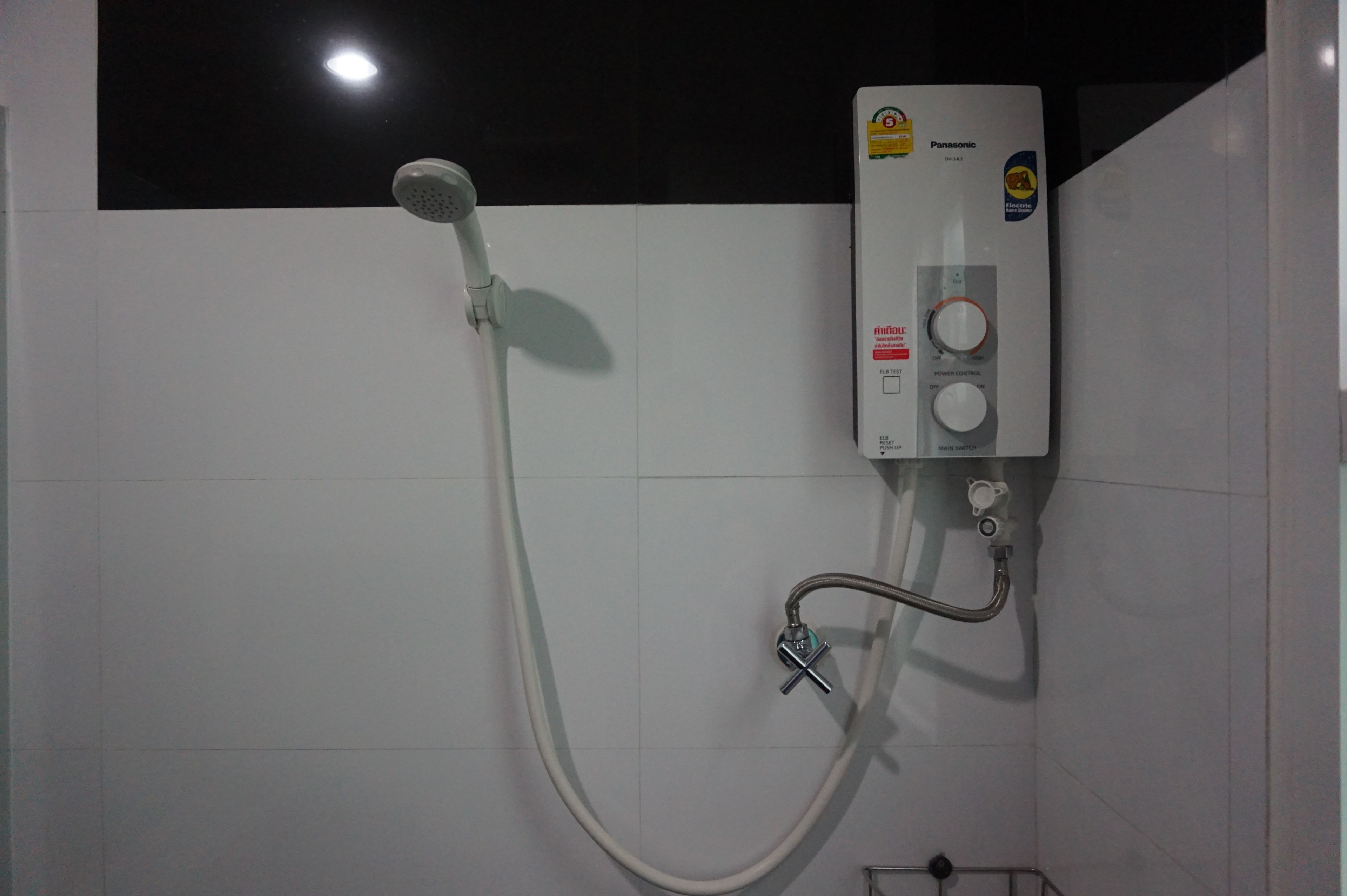 A bathroom with a white tiled wall, a handheld showerhead, and a wall-mounted control panel.