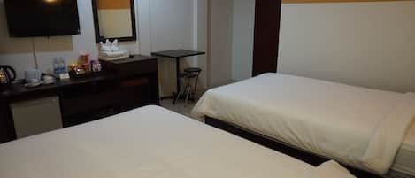 A hotel room with two single beds, a desk with a chair, a flat-screen TV, a mirror, and a small table with two stools.