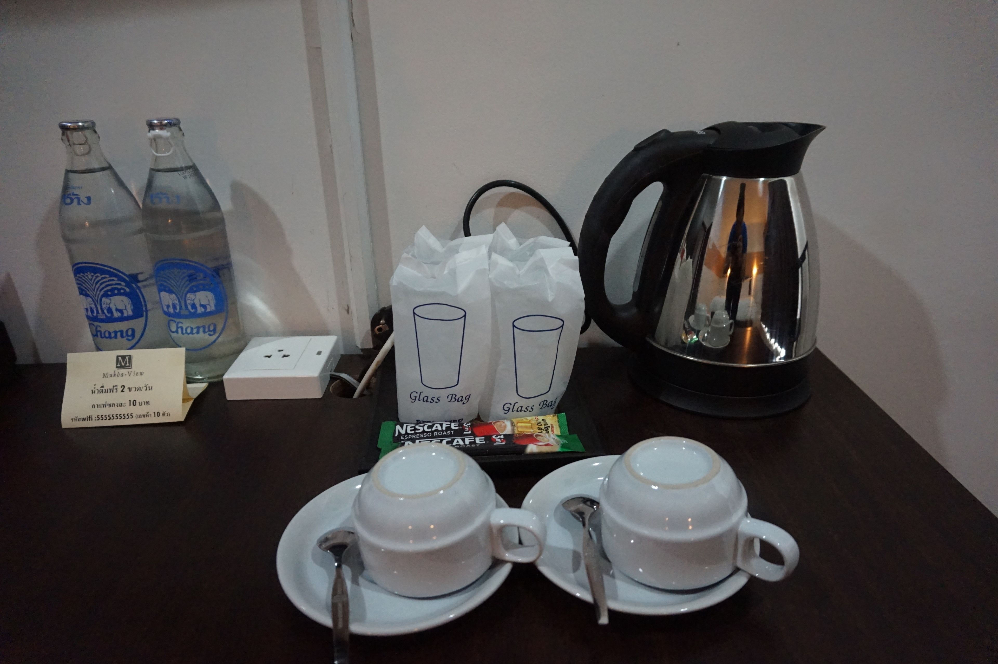 A table with two glass bottles, a coffee pot, two glass bags, a box, and two cups with saucers.