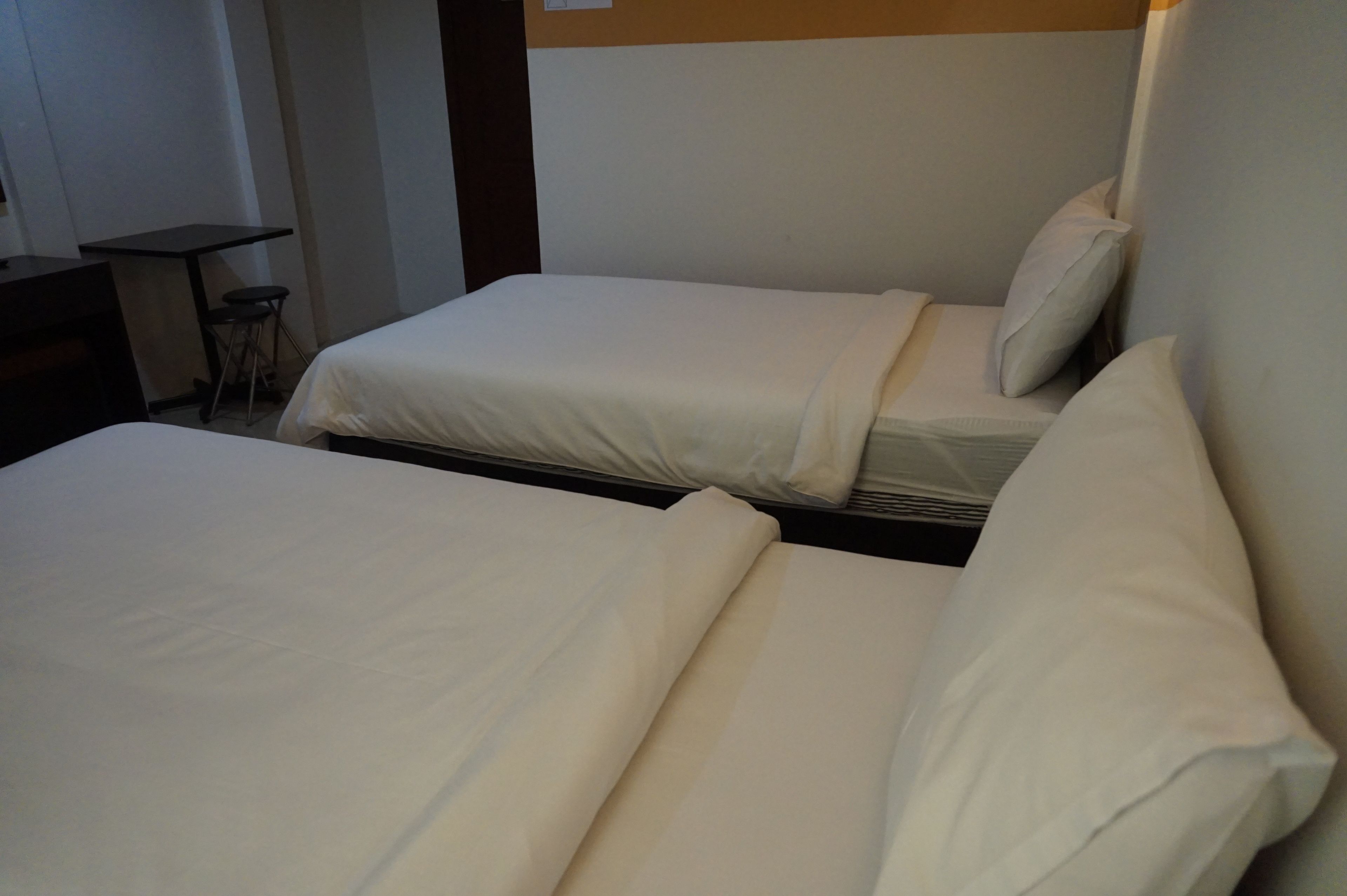 Deux lits simples avec du linge de lit blanc dans une chambre d’hôtel.