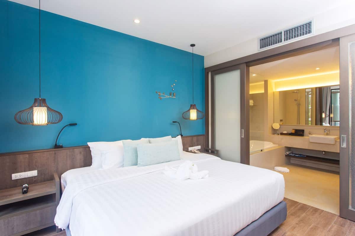 A modern hotel room with a large bed, a bathroom with a mirror and sink, and a blue accent wall.
