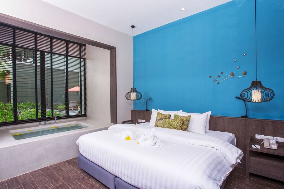 A modern hotel room with a large bed, a bathtub, and a view through floor-to-ceiling windows.