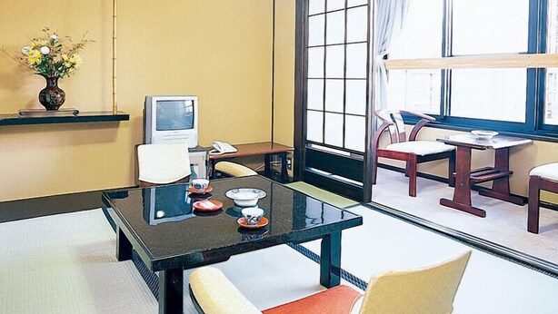 A traditional Japanese-style room with tatami flooring, a low table with a television, a vase with flowers, and a view through large shoji screens. - Gero Onsen Tsurutsuru no Yu Minorisou (Gero)