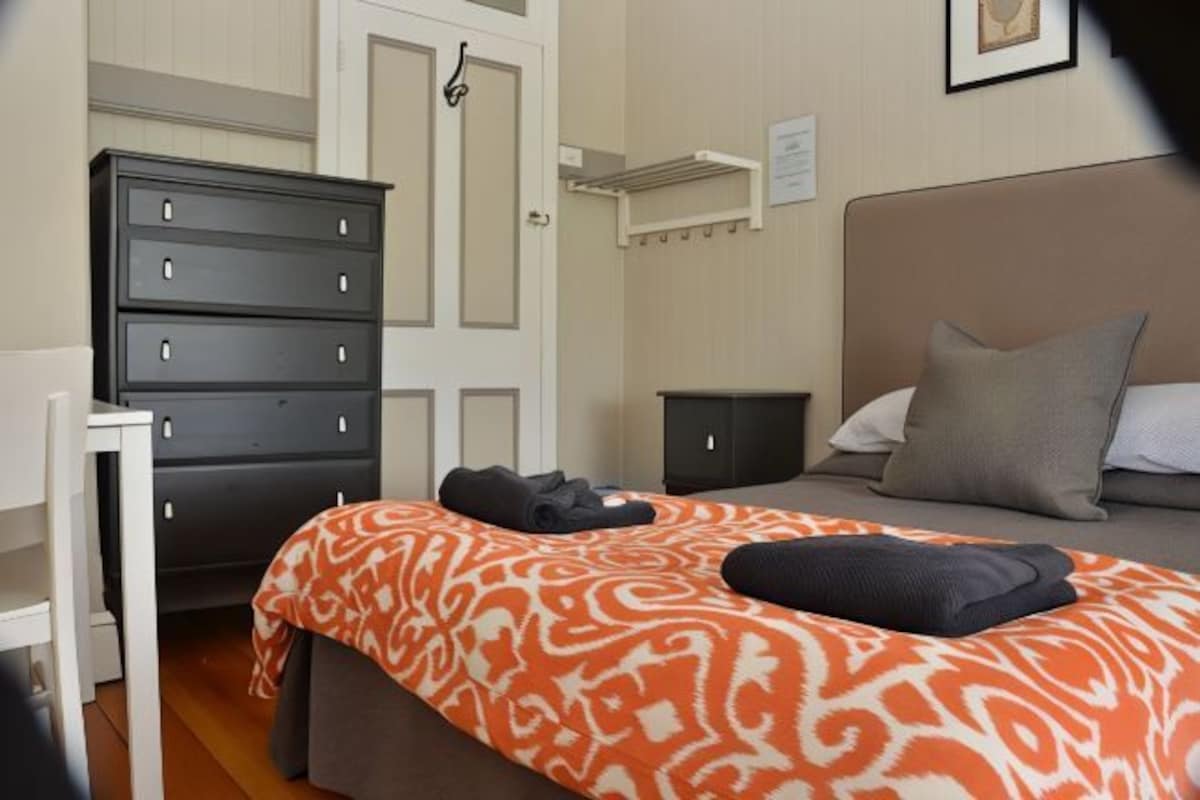 Un dormitorio con cama, cómoda, mesita de noche y estante en la pared.
