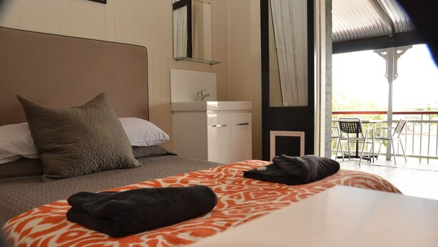 Quarto de hotel com uma cama, mesa de cabeceira, espelho, janela e varanda com cadeiras.