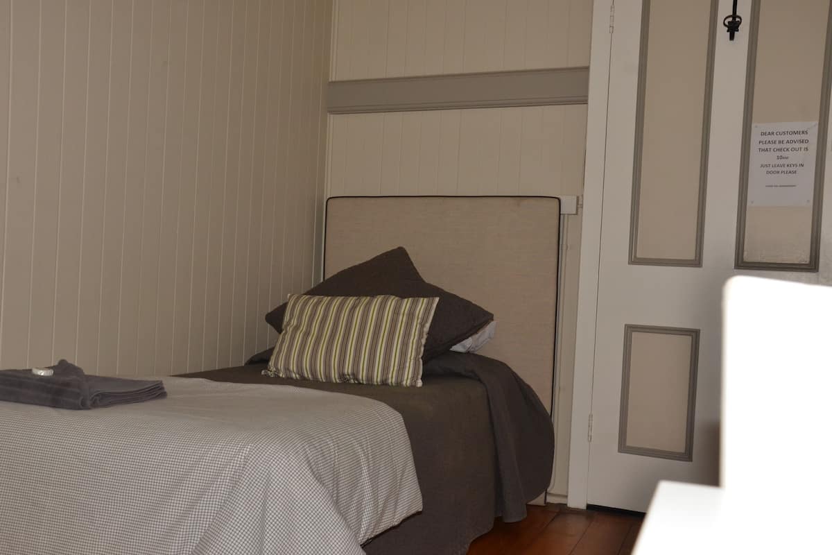 Habitación de hotel con cama, toalla doblada y un cartel en la puerta que indica a los huéspedes dejar las llaves puestas.