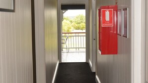 Um corredor com um extintor preso na parede, uma porta que dá para área externa e um quadro emoldurado na parede.
