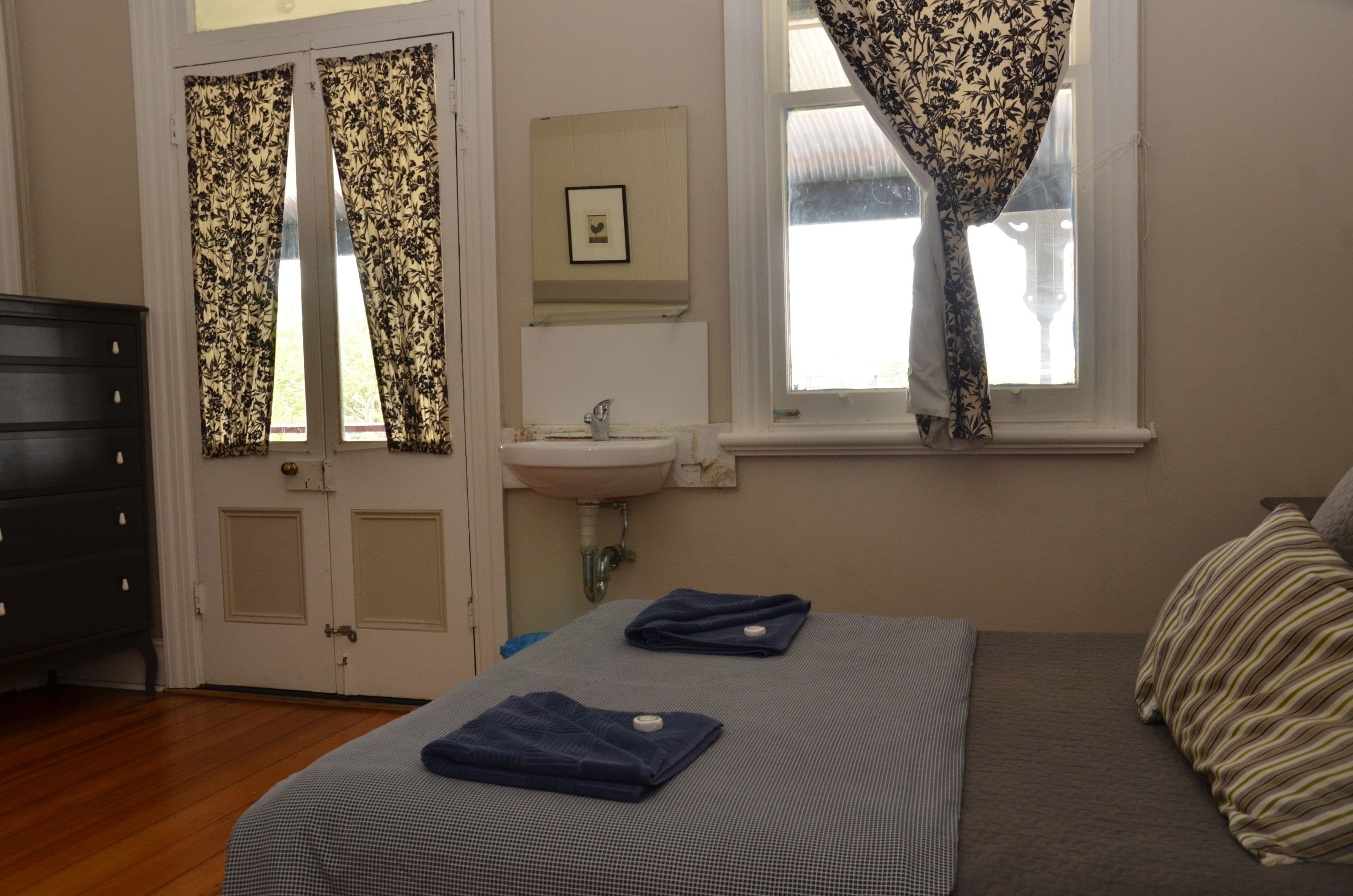 A bedroom with a bed, a dresser, a window with curtains, a sink, and a framed picture on the wall.