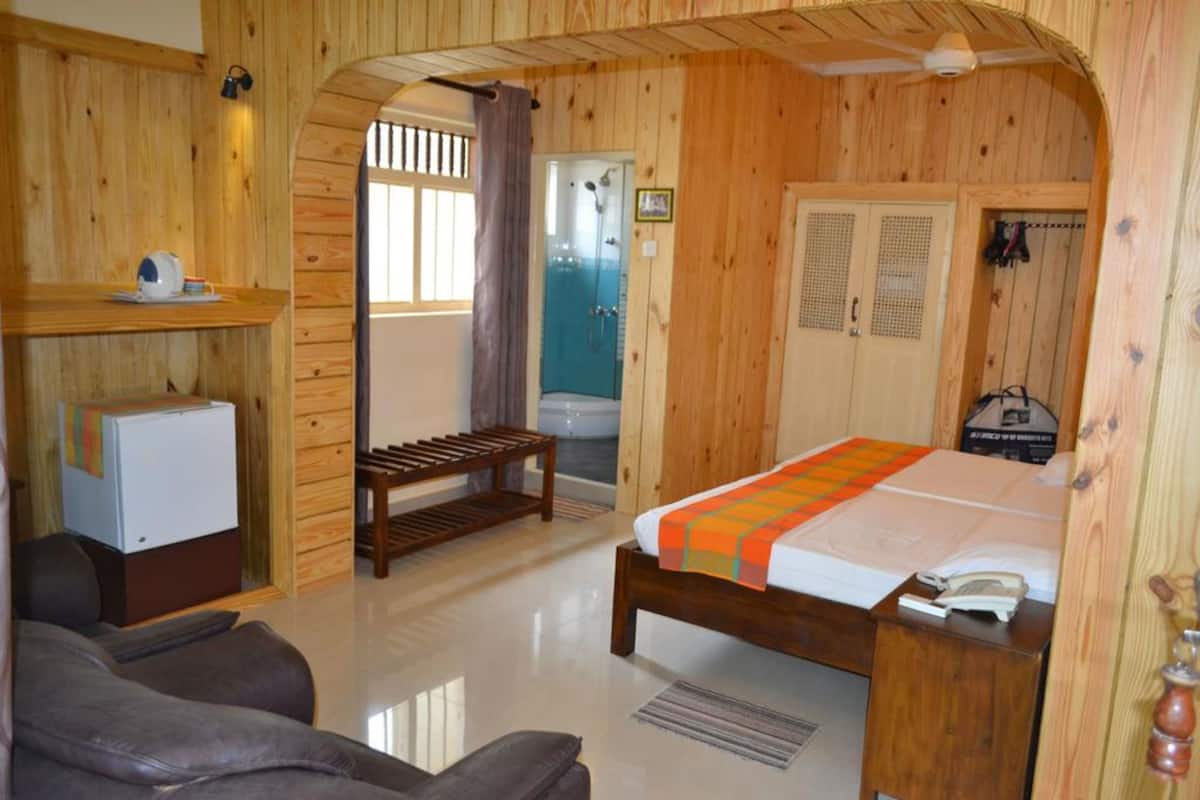 A wooden room with a bed, a small desk, a bench, and a shower area.