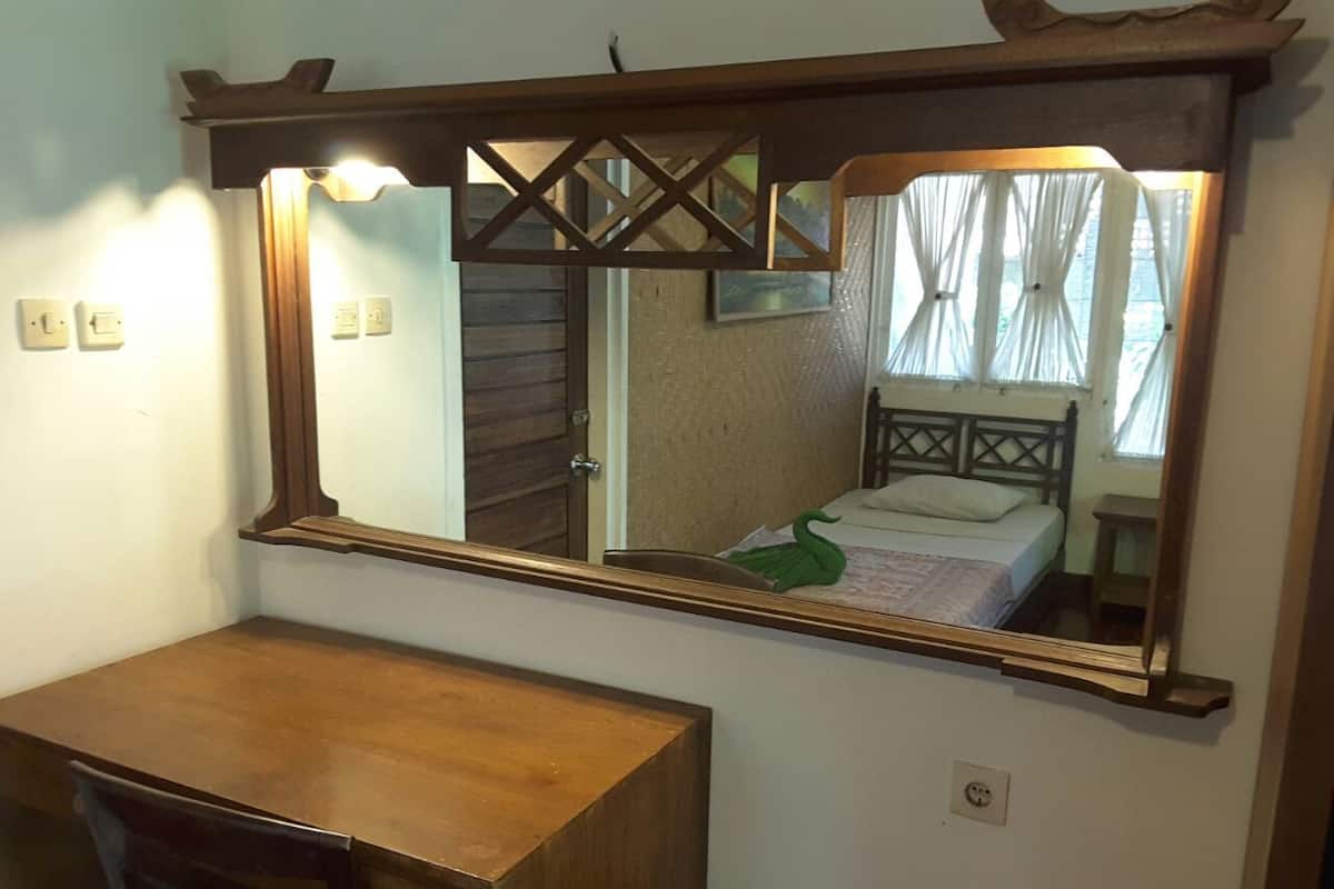 A wooden desk with a mirror above it, reflecting a bed with a green swan decoration.