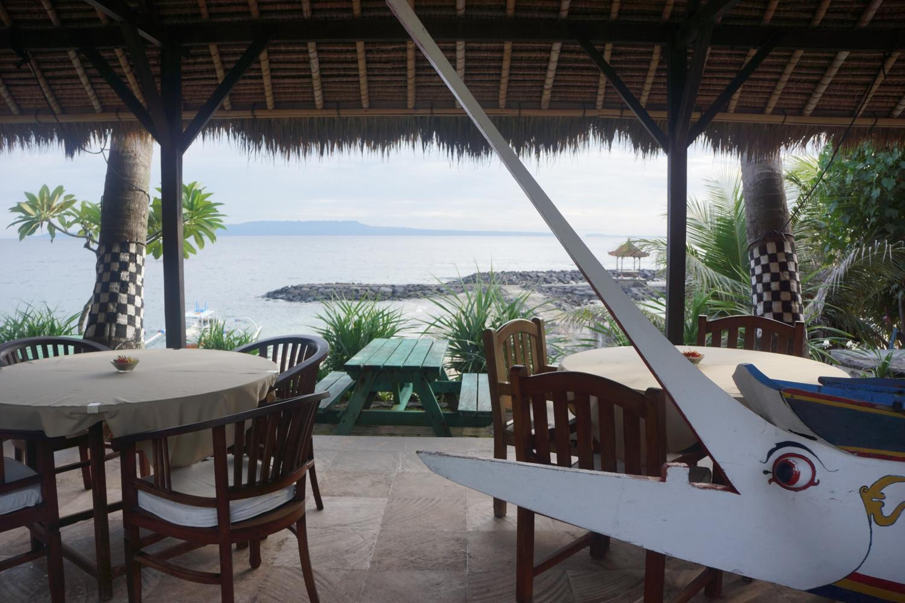 An outdoor seating area with tables and chairs, overlooking a body of water and a rocky shoreline.