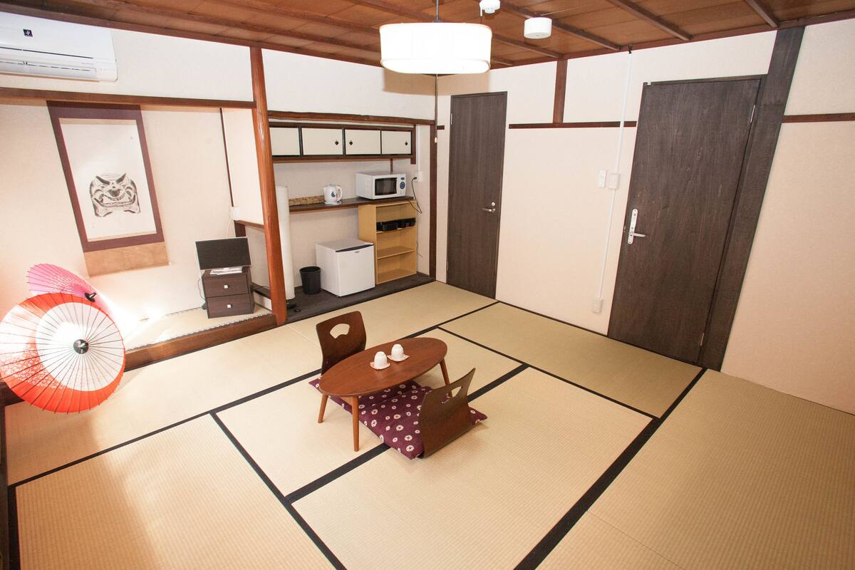 A traditional Japanese room with tatami flooring, a low table with two chairs, a fan, a microwave, and a cabinet.