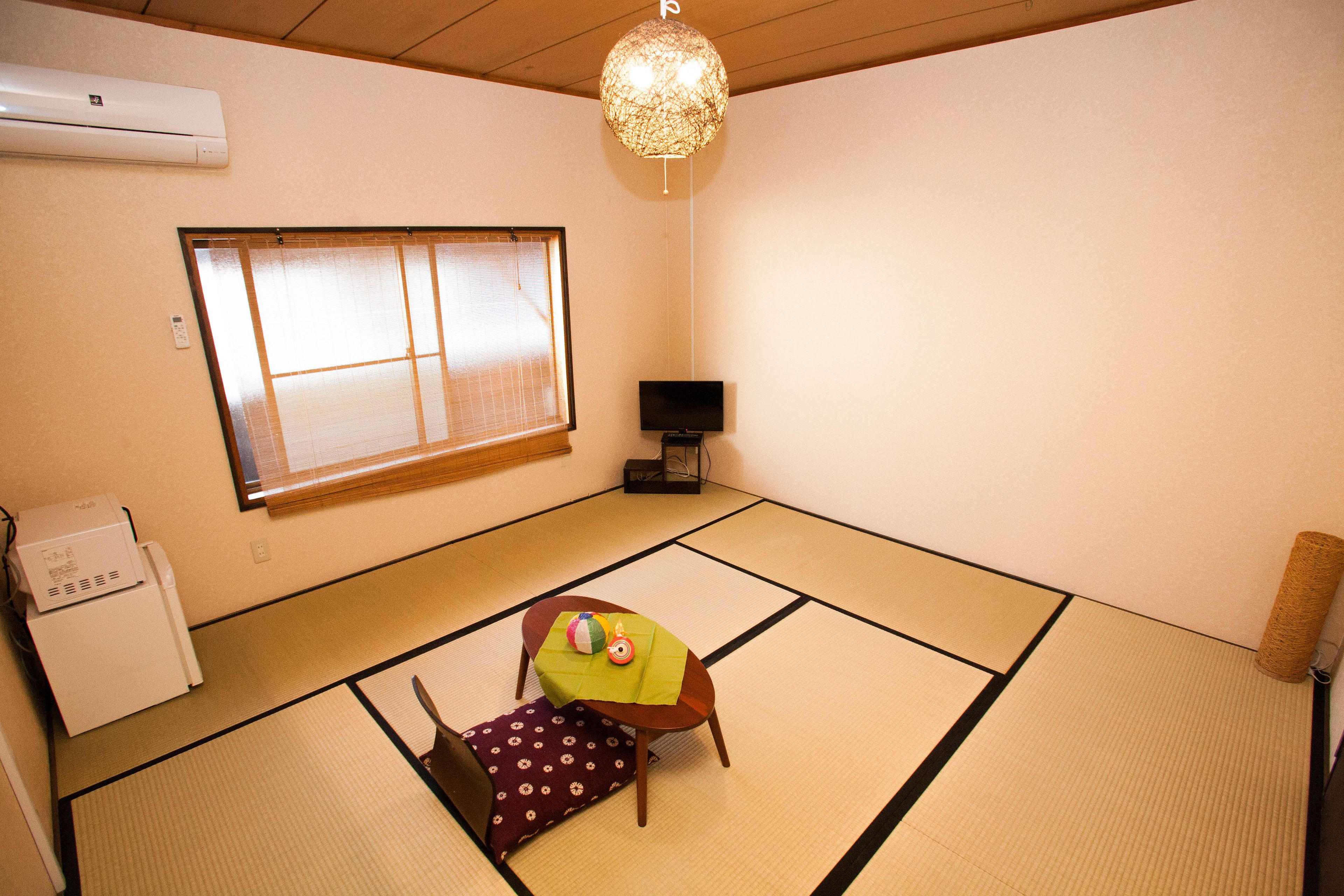 Una stanza con tatami, un futon, un tavolino ricoperto da una tovaglia verde, una televisione e un termosifone.