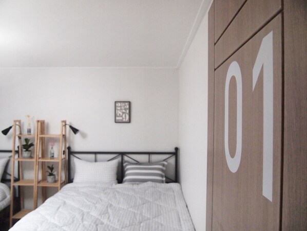 A bedroom with a bed, a wooden wardrobe with the number 01, a bedside table, a lamp, and a shelf with decorative items.