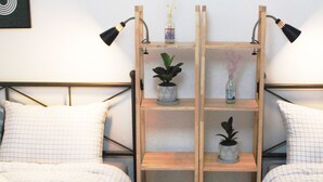 Un dormitorio con dos camas, cada una con almohadas a rayas, un estante de madera con plantas y una lámpara de pared.