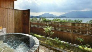 A hot tub with a stone edge, a wooden deck, and a view of a lake and mountains.