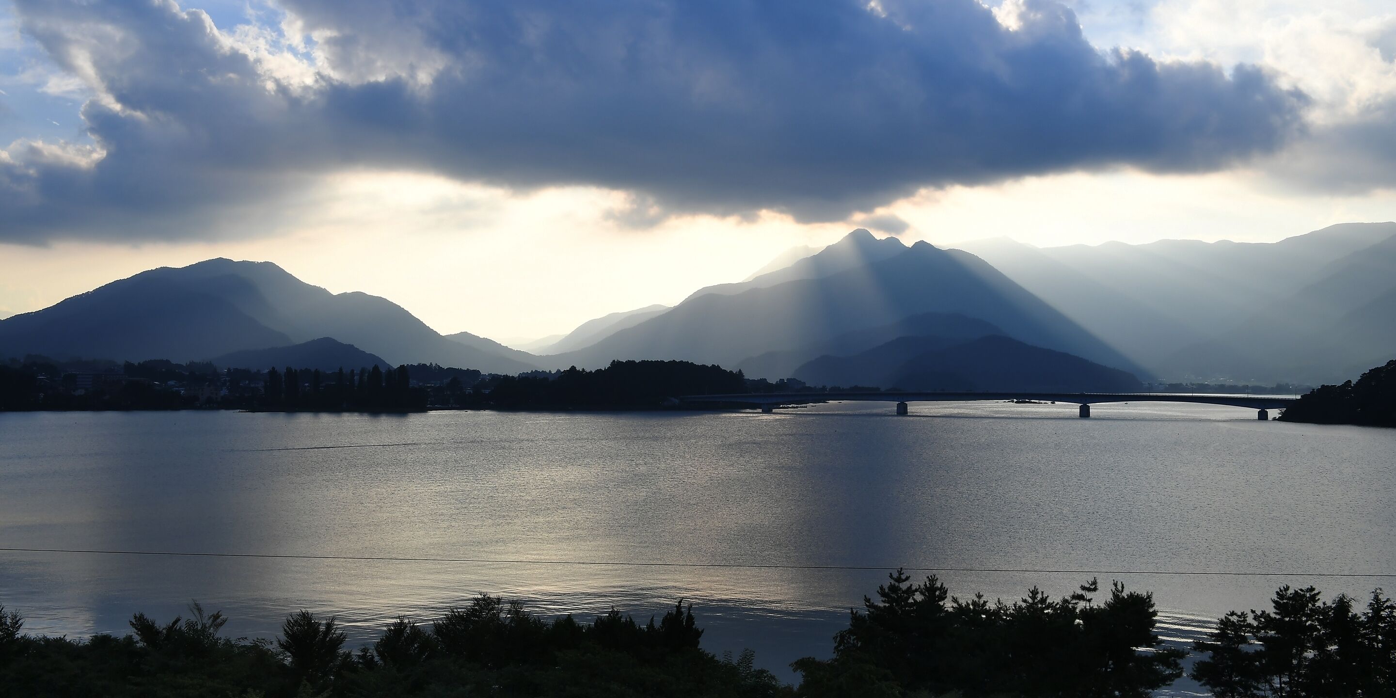 Un lago tranquilo con montañas al fondo y un puente que lo cruza.