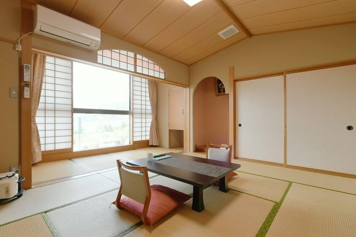 Una habitación japonesa tradicional con suelo de tatami, una mesa baja, una silla y puertas correderas.