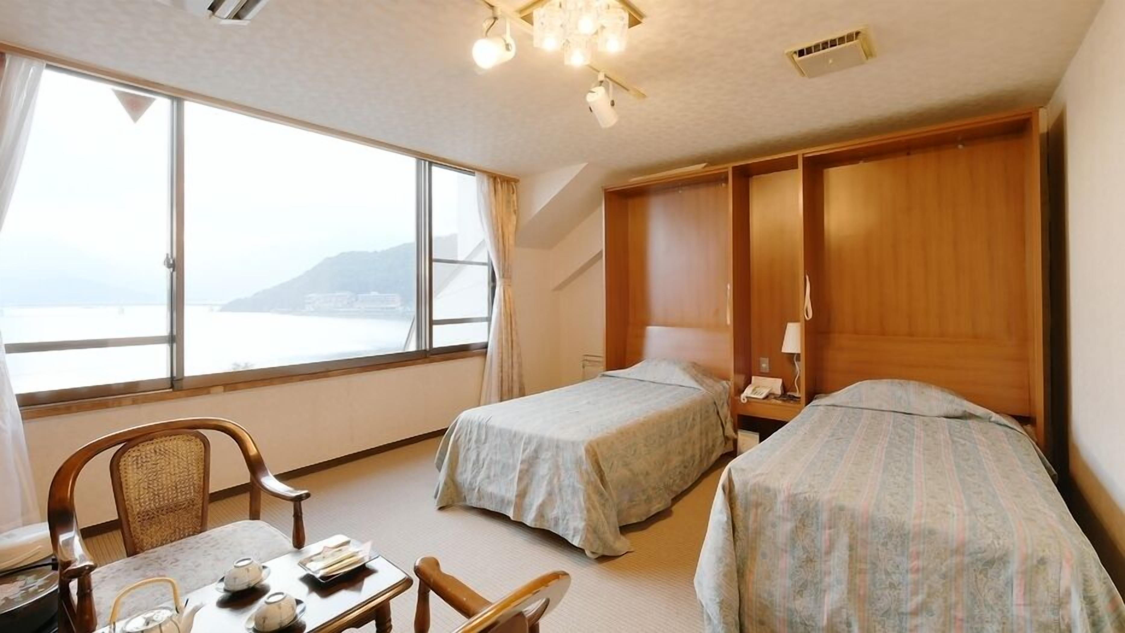 Habitación de hotel con dos camas, un escritorio con silla, una ventana con vistas al mar y un armario de madera.