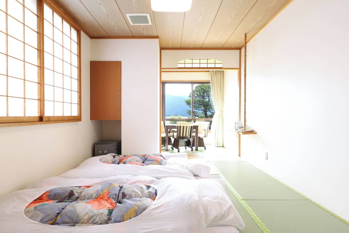 A traditional Japanese-style room with tatami flooring, a futon bed, a wooden cabinet, and a view of the outdoors.