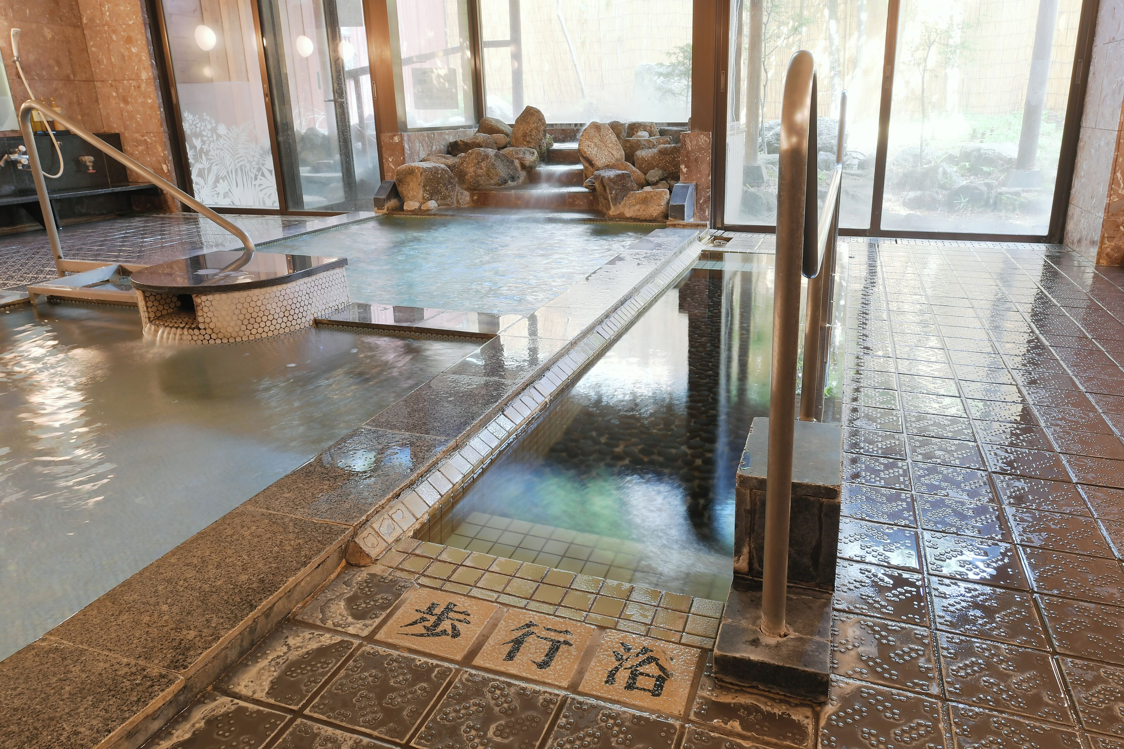 Un onsen japonés tradicional con un baño de piedra, un banco de madera y un suelo de baldosas con caracteres japoneses.