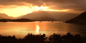 A sunset over a calm lake with mountains in the background and a bridge crossing the water. - Hotel Koryu (Fujikawaguchiko)