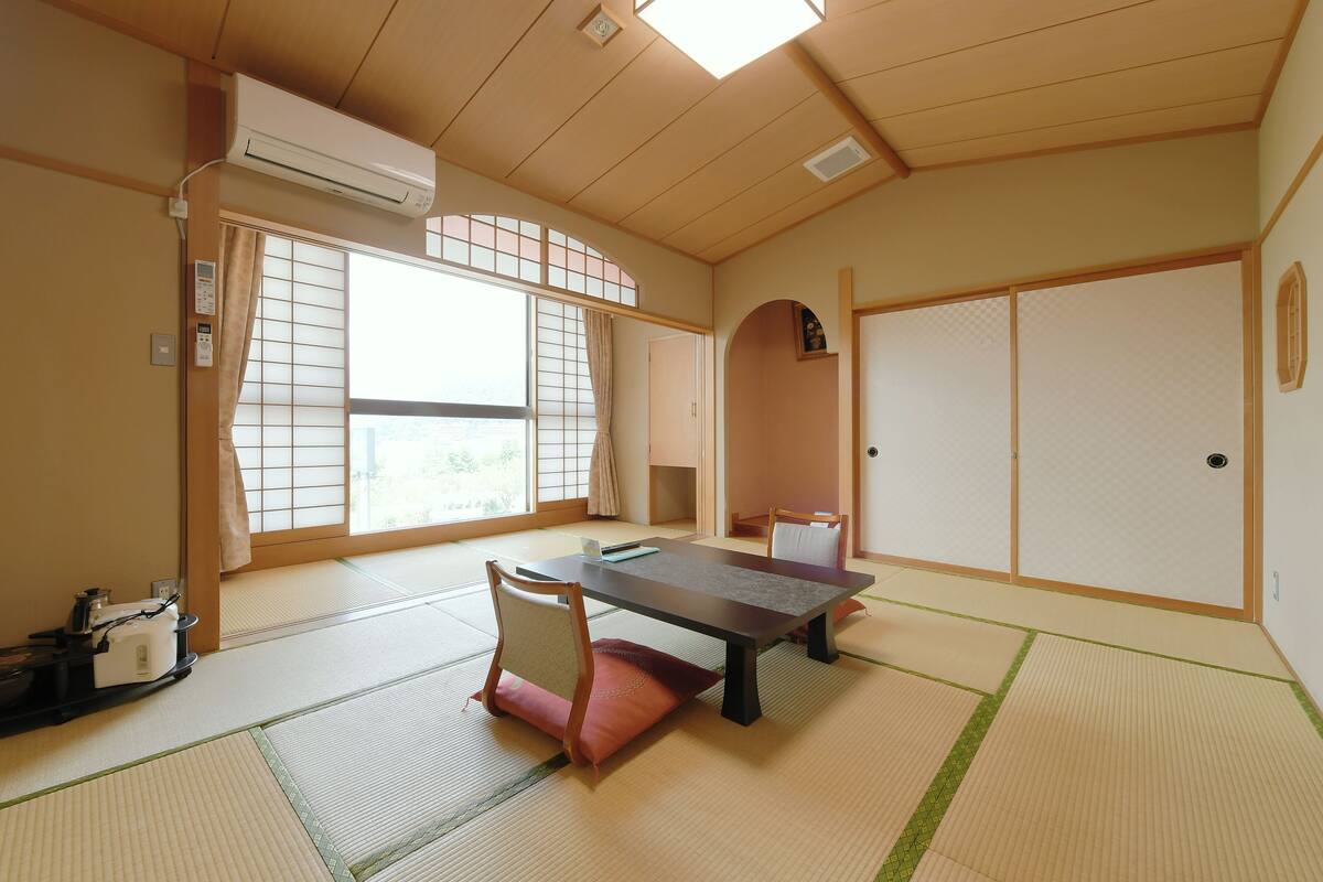 A tatami mat room with a low table, chairs, and sliding doors.