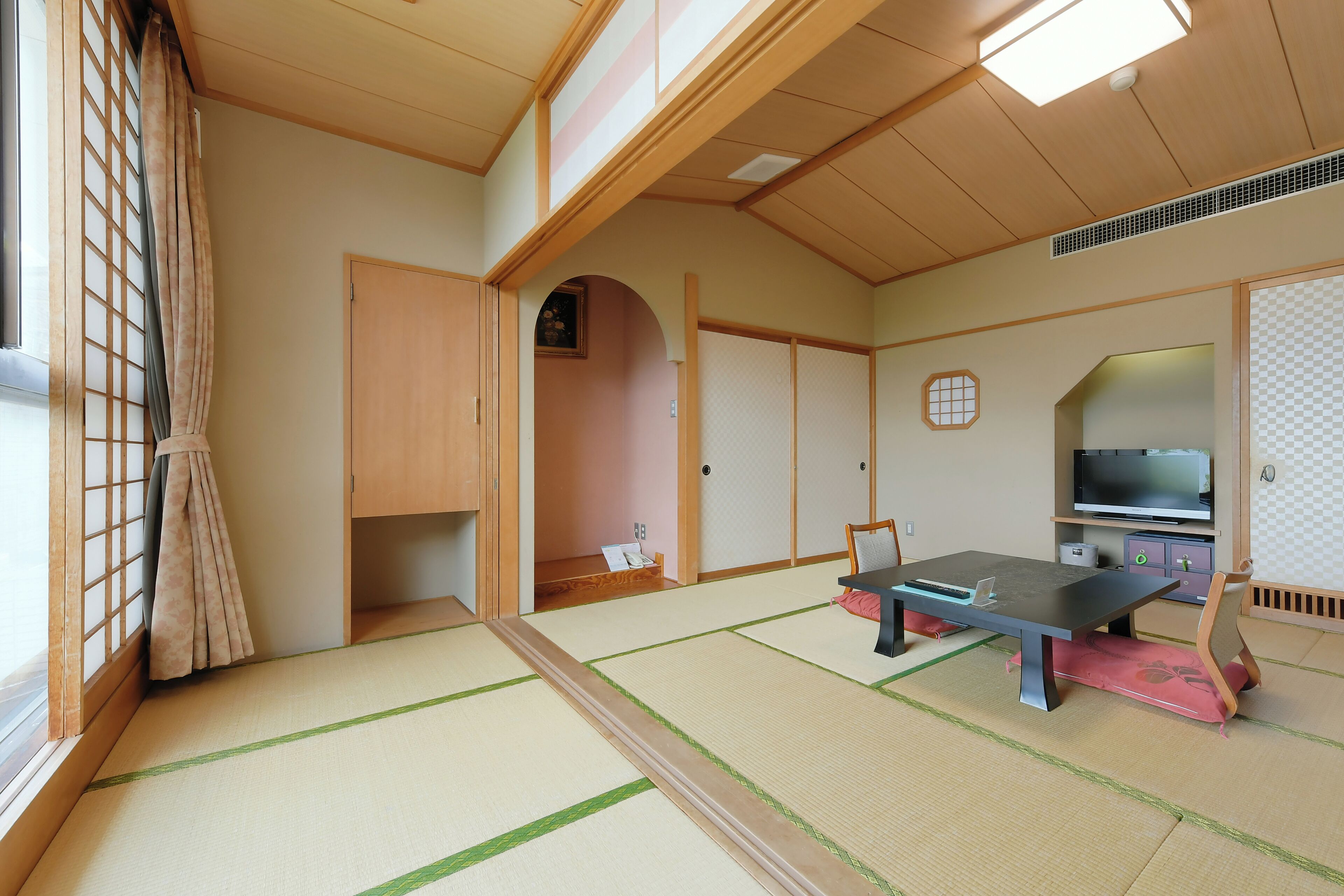 Una habitación japonesa tradicional con suelo de tatami, una mesa baja con cojines, un televisor y puertas correderas.