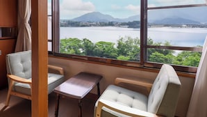 A room with a large window offering a view of a lake and mountains. There are two chairs and a small table.