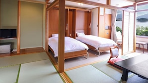 A traditional Japanese-style room with tatami flooring, two single beds, a wooden wardrobe, a television, and a view of a lake.