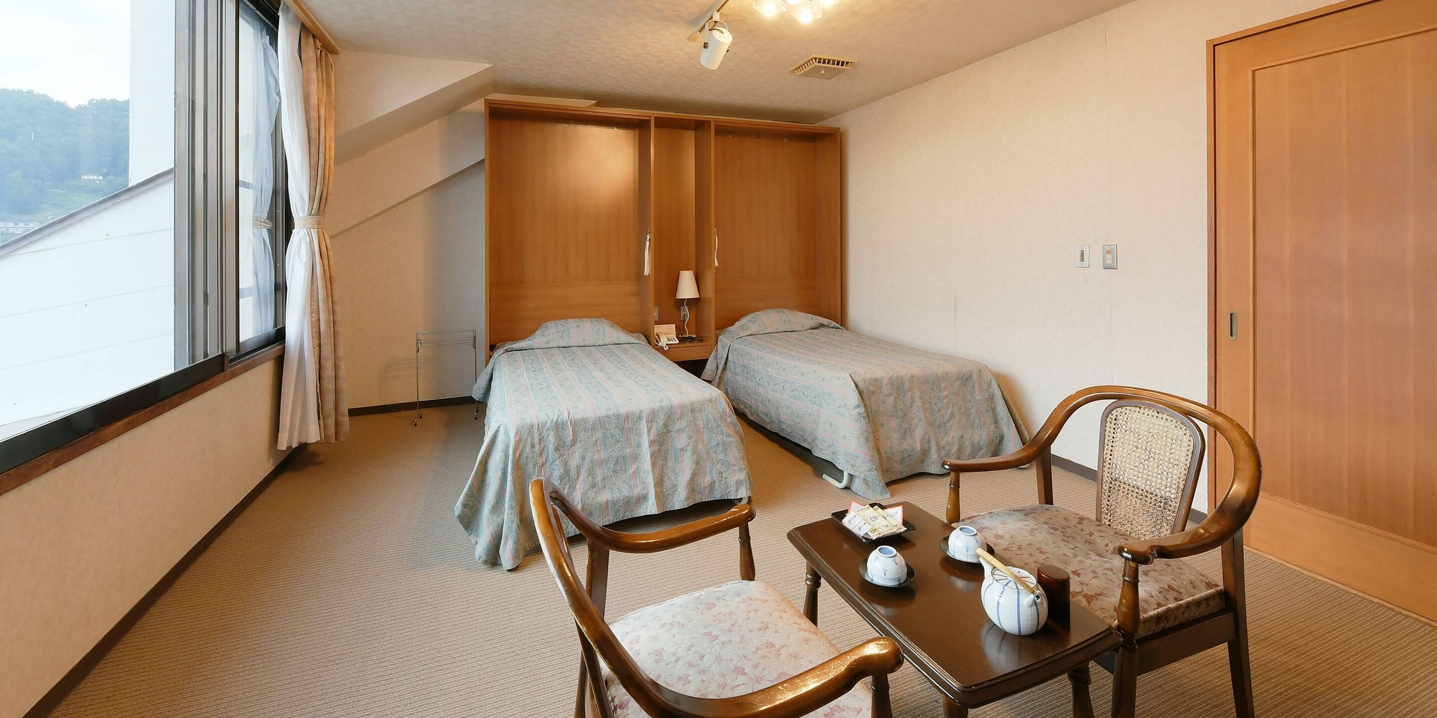 Ein Hotelzimmer mit zwei Betten, einem Holzschrank, einem kleinen Tisch mit Tee-Zubehör und Blick ins Freie.