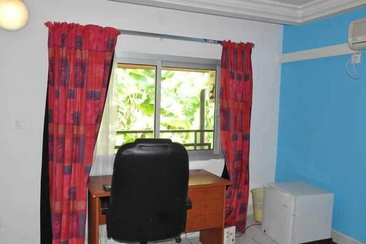 Een kamer met een bureau, stoel en een raam met gordijnen.