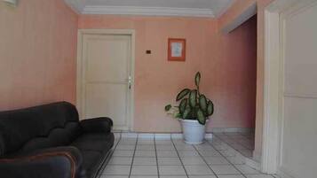 A room with a black sofa, a white door, a potted plant, and a tiled floor.