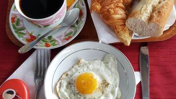 Un plateau de petit-déjeuner avec des croissants, un œuf au plat, du beurre, de la confiture et une tasse de café.