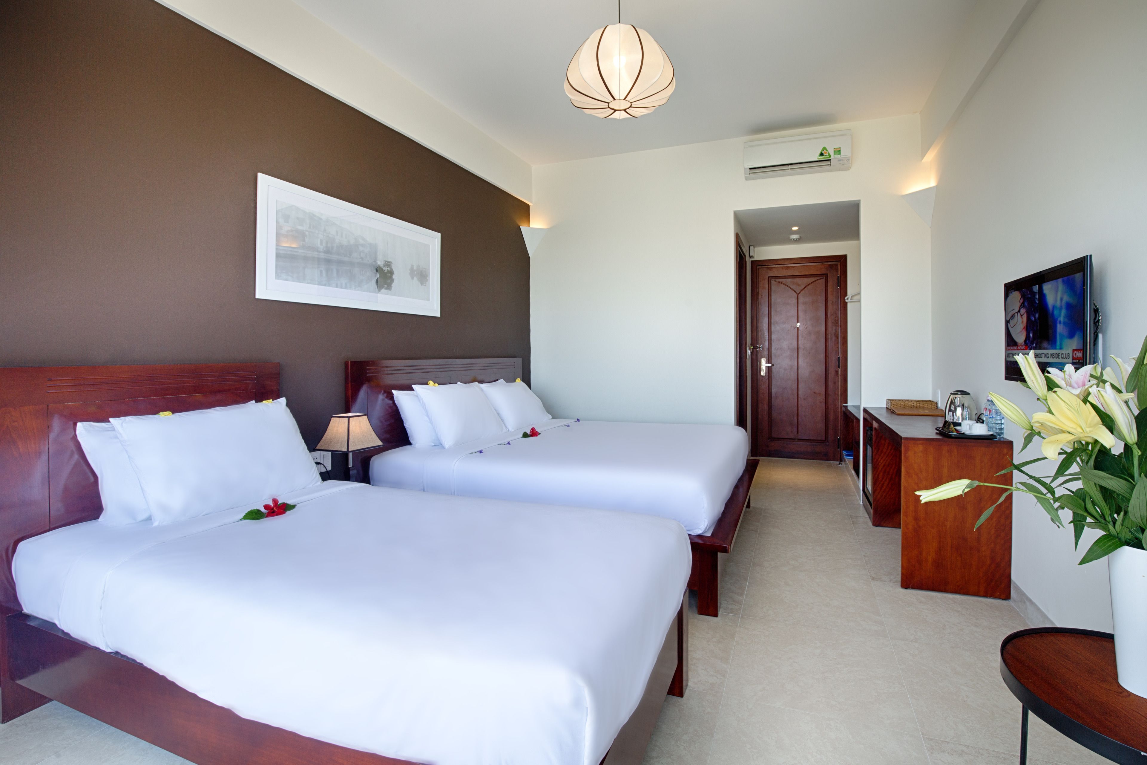 A hotel room with two beds, a desk, a chair, a TV, and a framed picture on the wall.