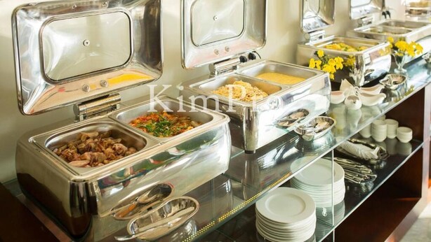 A buffet with various food items in metal containers, a glass counter, and stacked white plates.