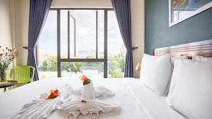 Habitación de hotel con una cama grande, vista de la ciudad por la ventana y una silla verde junto a la ventana.