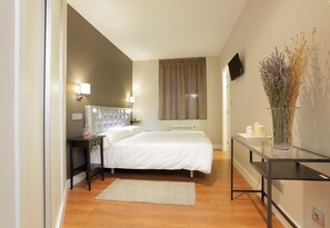 A bedroom with a bed, bedside tables, a nightstand, a TV, a window with curtains, and a vase with dried flowers. - Hotel Rosal (Oviedo)