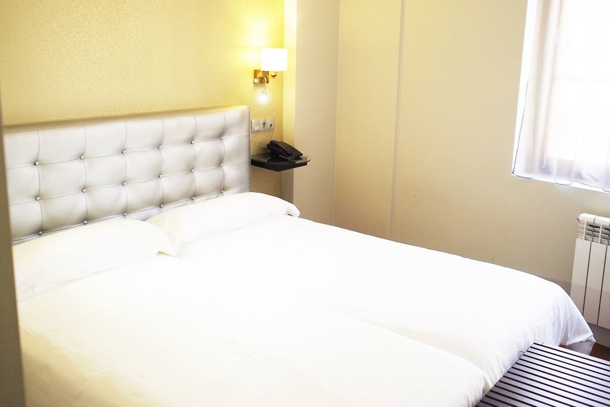 A neatly made bed with a tufted headboard, a bedside telephone, and a wall-mounted light fixture.