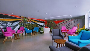 A modern lobby with colorful chairs, a reception desk, and a vibrant mural on the wall. - favehotel Kuta Kartika Plaza (Kuta)