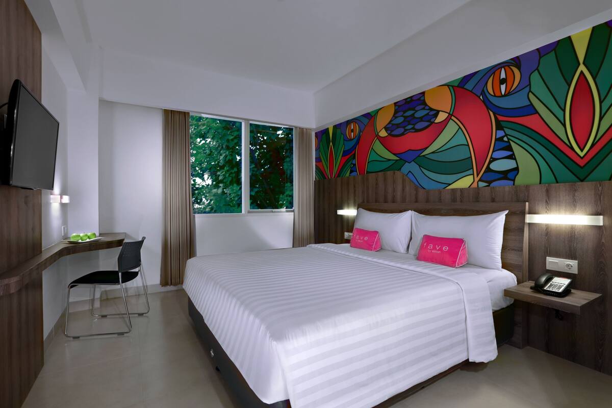 Habitación de hotel con una cama grande, un escritorio con silla, un televisor y un mural colorido en la pared.