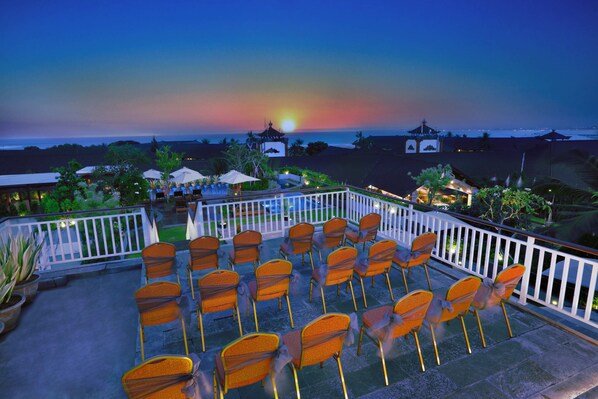Una terraza con sillas dispuestas para comer, con vista a un atardecer.