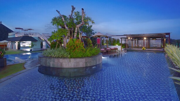 A swimming pool with tiled flooring, surrounded by lounge chairs and a covered seating area. - favehotel Kuta Kartika Plaza (Kuta)