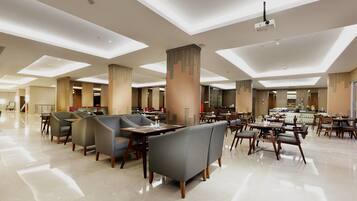 A spacious hotel dining area with multiple tables and chairs, a central bar, and a modern ceiling design.